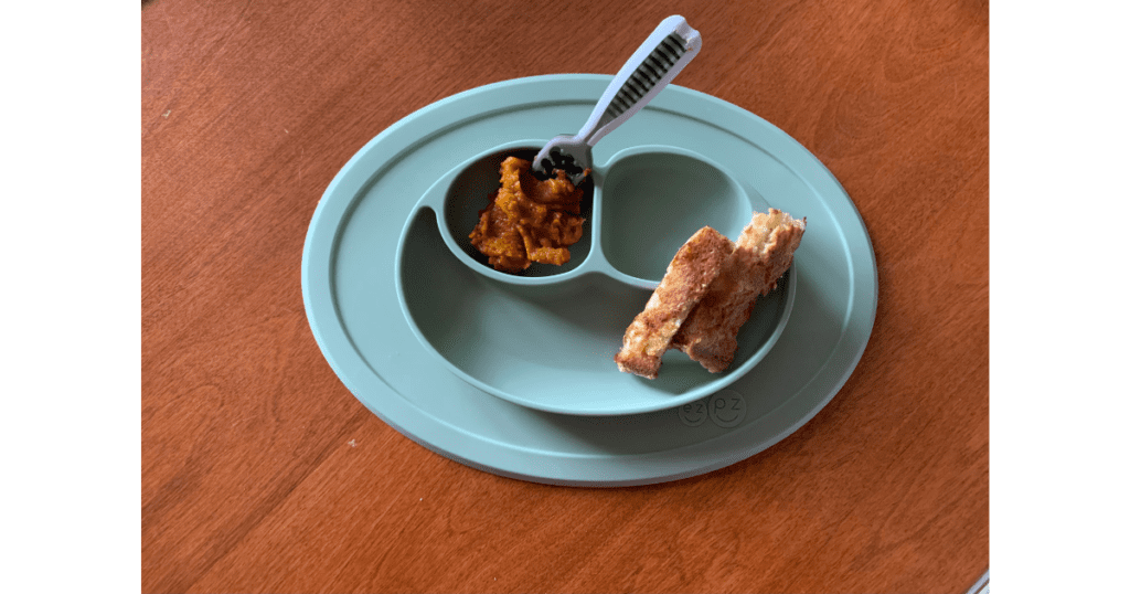 Kids mat on a wooden table with pumpkin puree on spoon and French toast in corner.