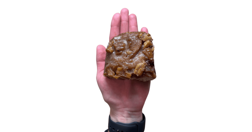 Hand holding sticky bun with pecans. Black wristwatch.