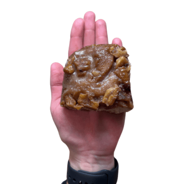 Hand holding sticky bun with pecans. Black wristwatch.