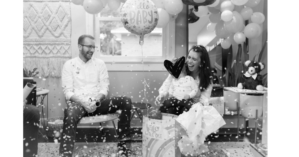 Family sitting under balloons and confetti with a 'hello baby' ballon. 