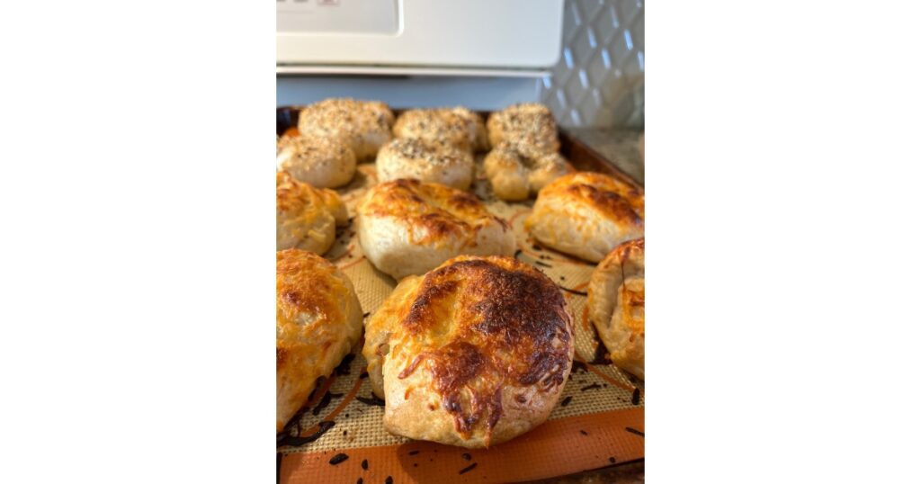 Asiago cheese bagels with everything bagels behind them. On a sheet pan.