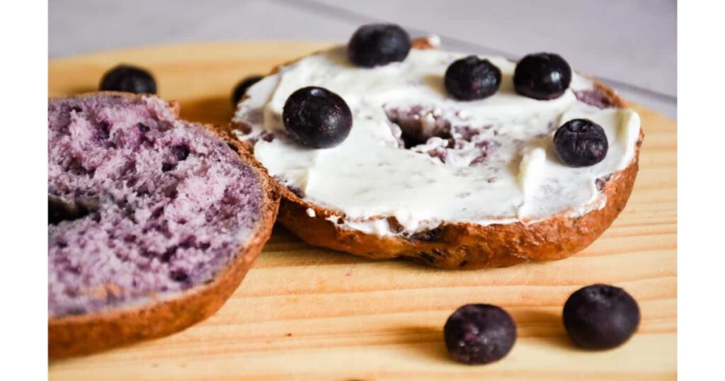 Blueberry sourdough bagel cut open with cream cheese and blueberries on top.