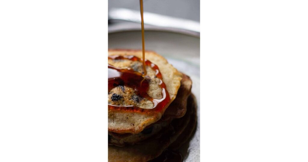 Blueberry pancakes with maple syrup drizzle coming down on top.