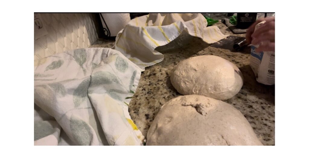 Two bread loaves on a countertop. Two towel lined bowls.