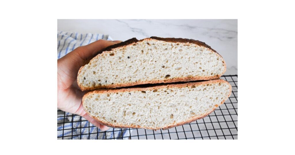 Bread loaf cut in half and held in air by hand. Over a blue and white towel with a cooling rack underneath.