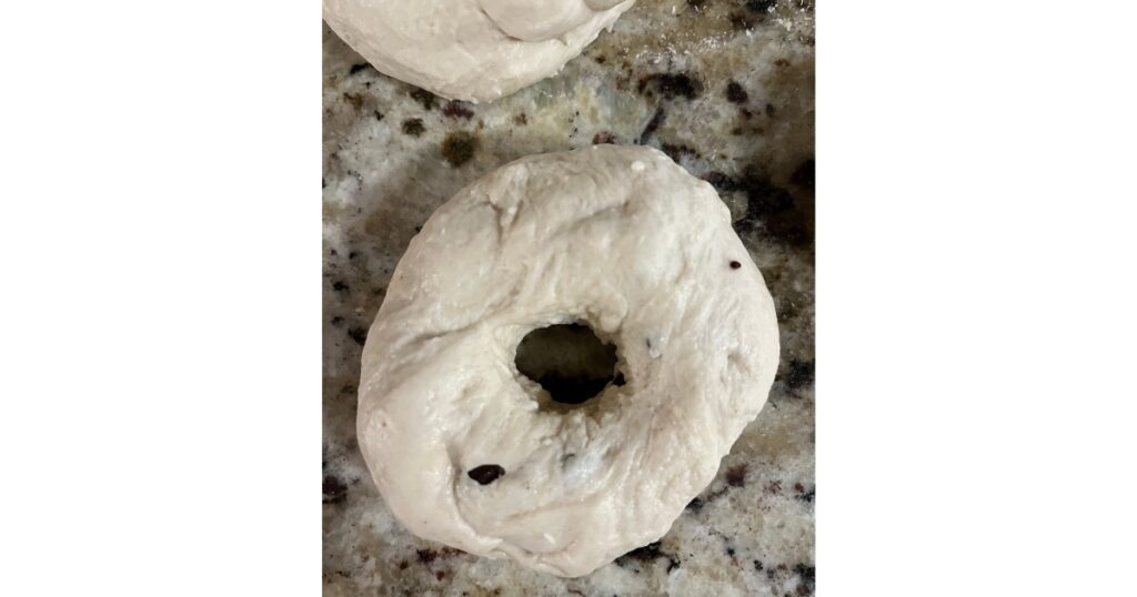 One bagel with two chocolate chips on a marble countertop.