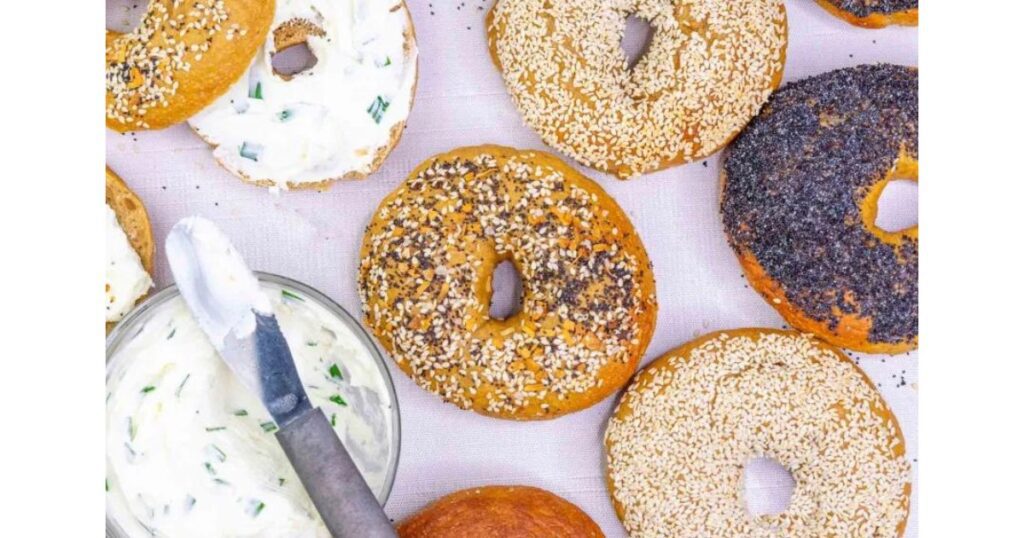 Bagels with spices and a few cut open with cream cheese