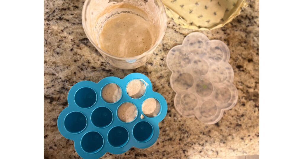 Sourdough starter with beeswax wrap and blue one ounce organizer with lid on granite countertop.