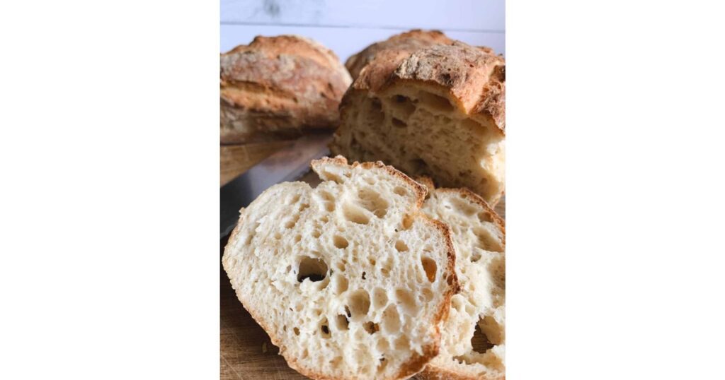 Bread loaf cut in half with a slice in front. Knife on table.