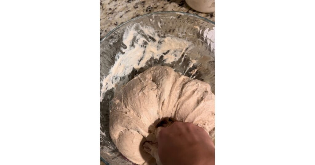 Hand kneading dough in a clear bowl.