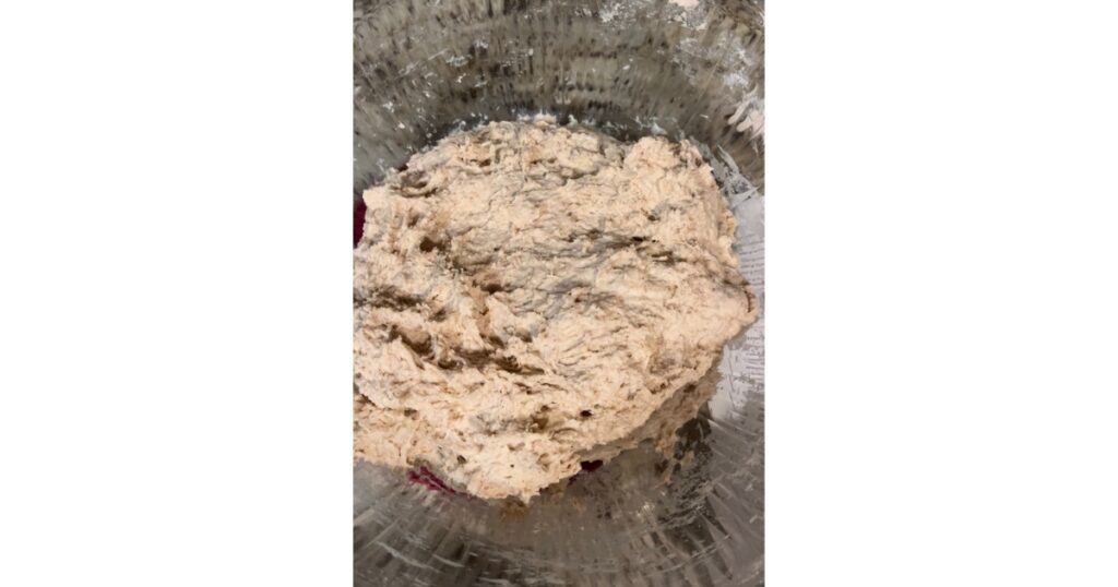 Bread dough sitting in a clear bowl.