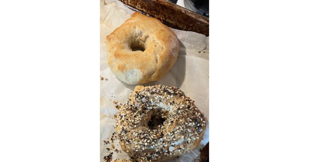 Two bagels on a sheet tray - one plain and the other with everything but the bagel seasoning.