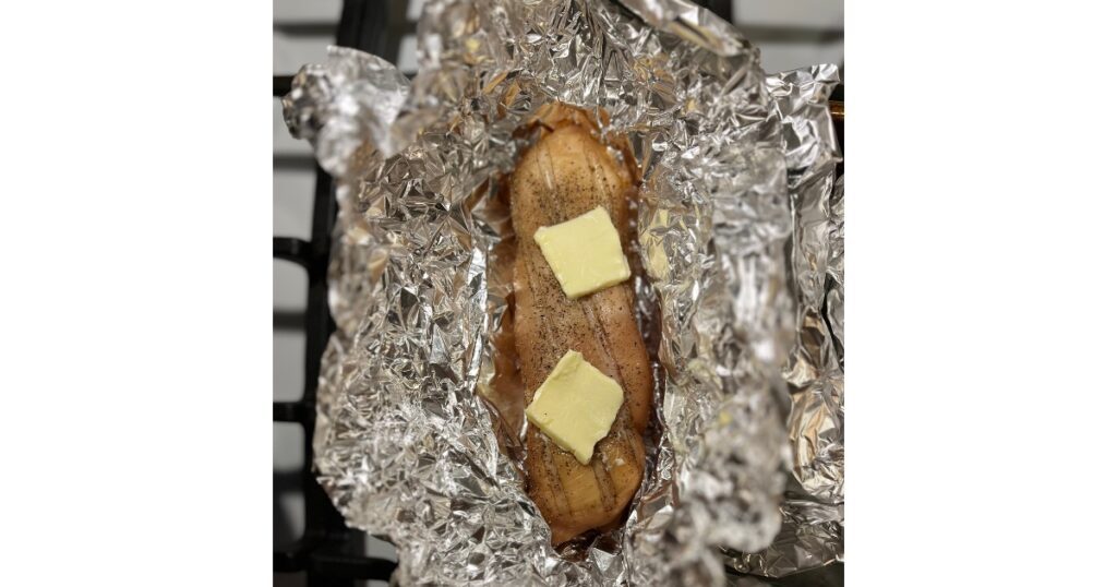 Chicken in aluminum foil and two slabs of butter placed on top.