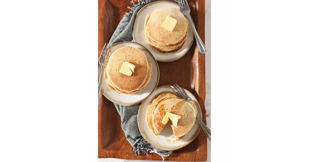 Three stacks of sourdough pancakes with butter on top. On a table and blue kitchen towel.