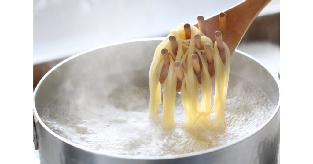 Sourdough pasta noodles being pulled out of boiling water with a wooden spoon.