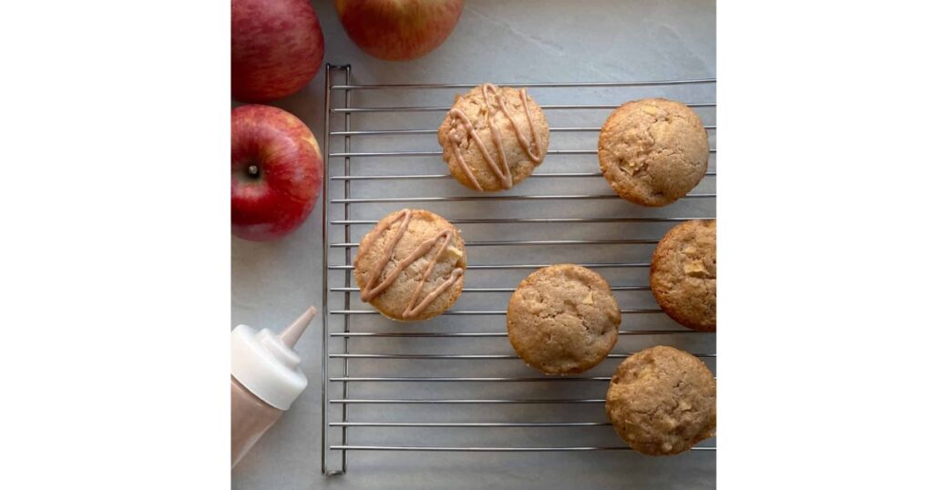 Apple muffins on a drying rack with three apples to the left