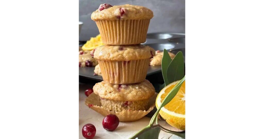 Cranberry orange muffins stacked with two cranberries and a halved orange