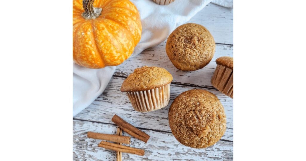 Four pumpkin muffins with a pumpkin in the left corner and cinnamon sticks
