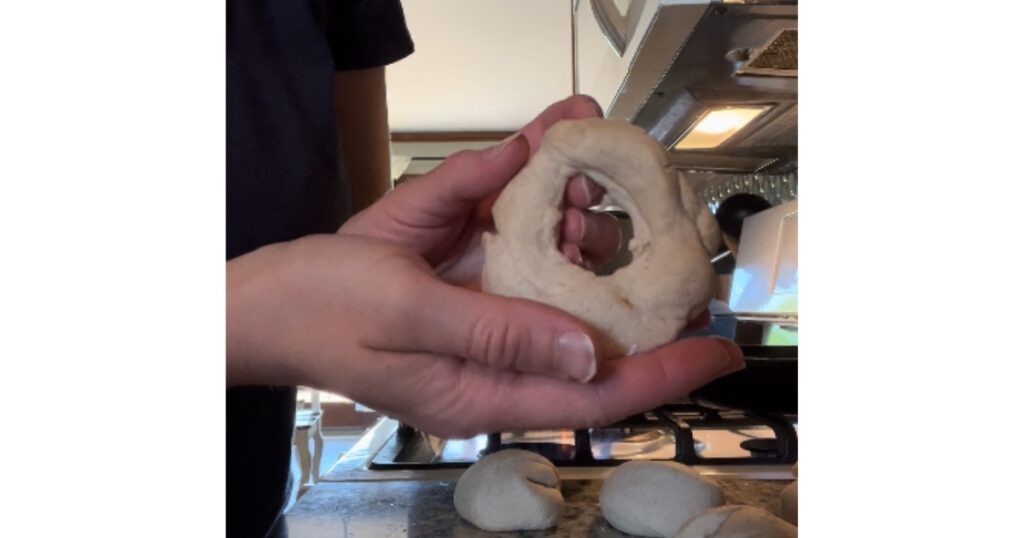 Formed bagel dough being held by hands