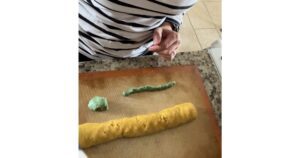 hands shaping orange and green cookie dough to make a pumpkin shape