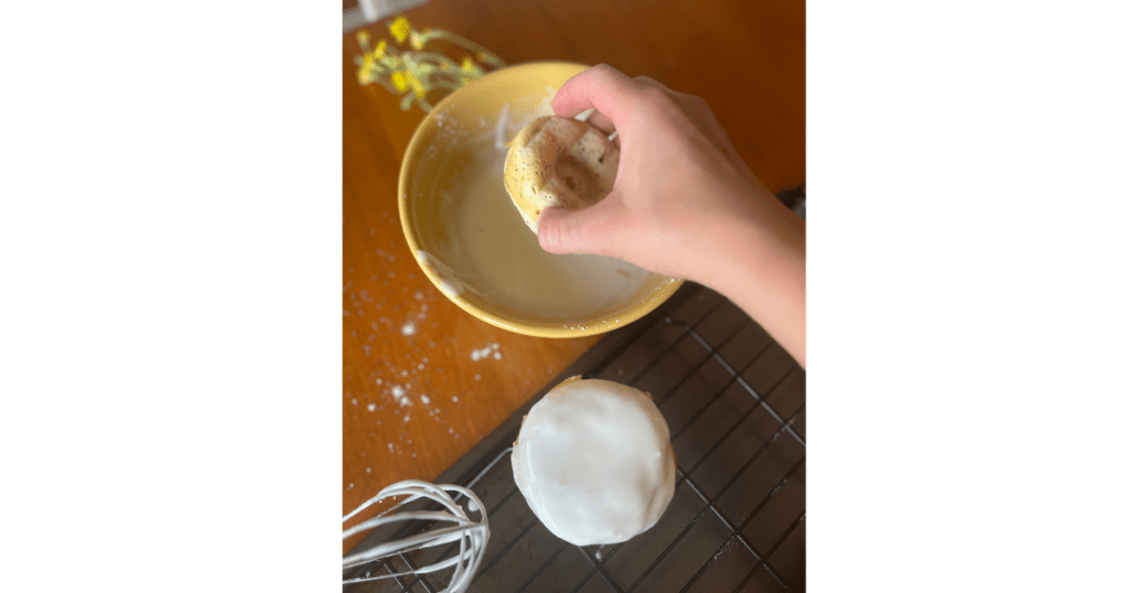 donut being dipped into a yellow bowl of lemon icing