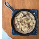 dutch baby with apples in a cast iron skillet on a polka dot place mat.