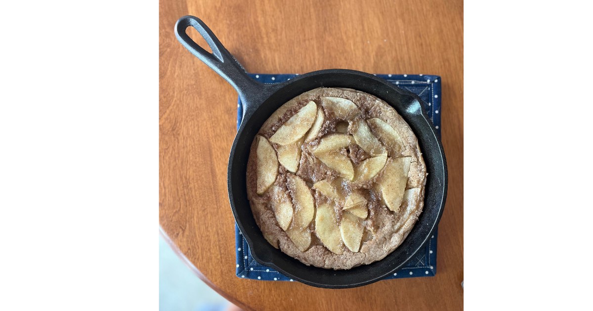 dutch baby with apples in a cast iron skillet on a polka dot place mat.