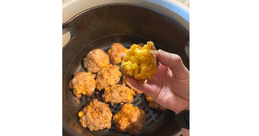 hand holding mac and cheese bite over mac and cheese bites in air fryer