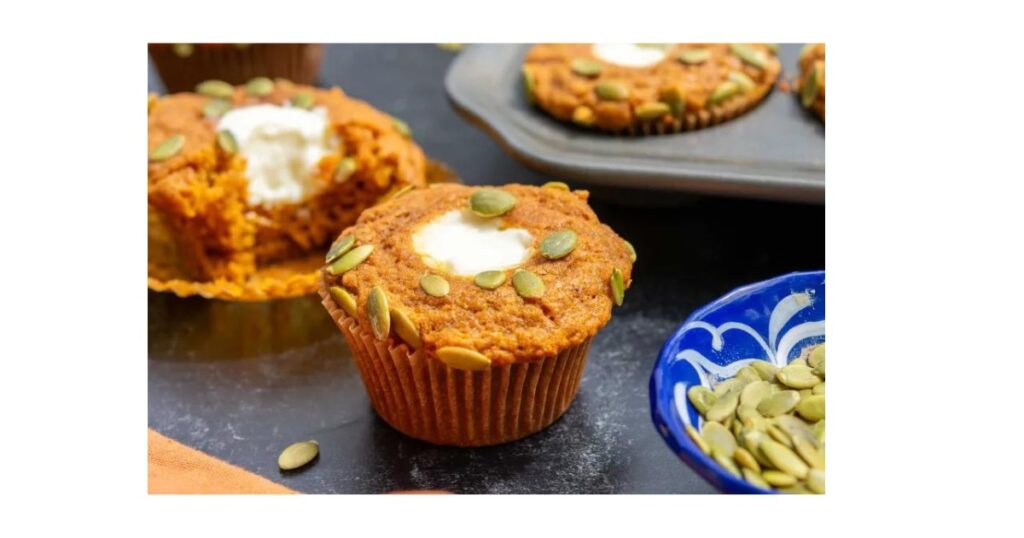 three pumpkin muffins with cream cheese in middle and pumpkin seeds on top