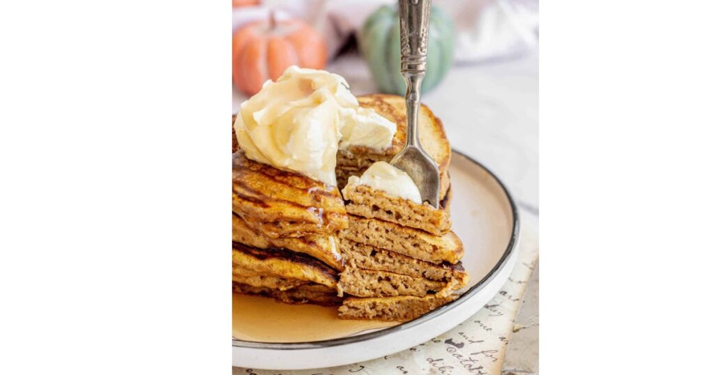 stack of pancakes with fork taking a slice out. Whipped cream on top