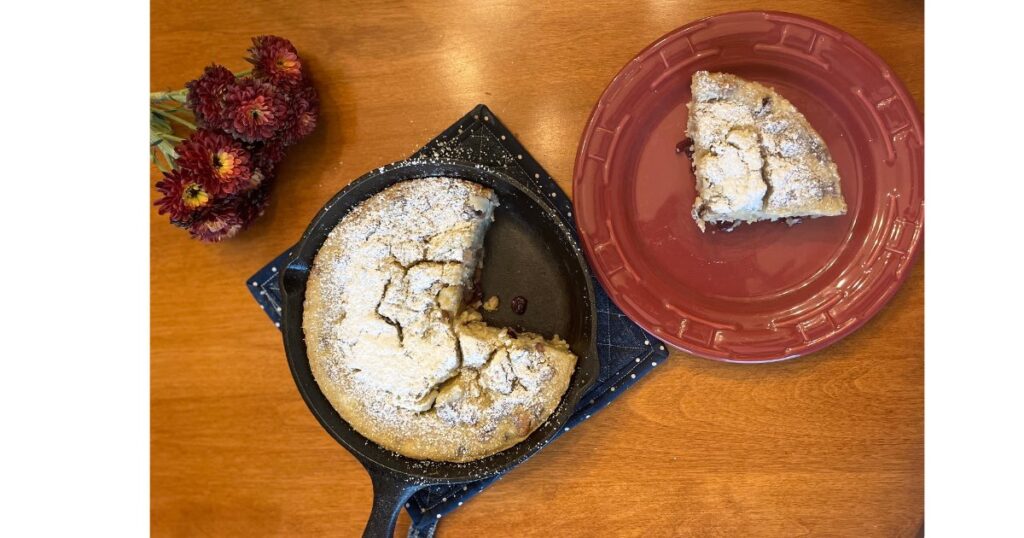 slice of sourdough dutch baby on a red plate and remainder in cast iron skillet