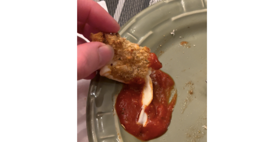 hand dipping mozzarella stick in pizza sauce