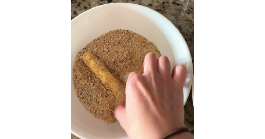 rolling mozzarella stick through breadcrumbs